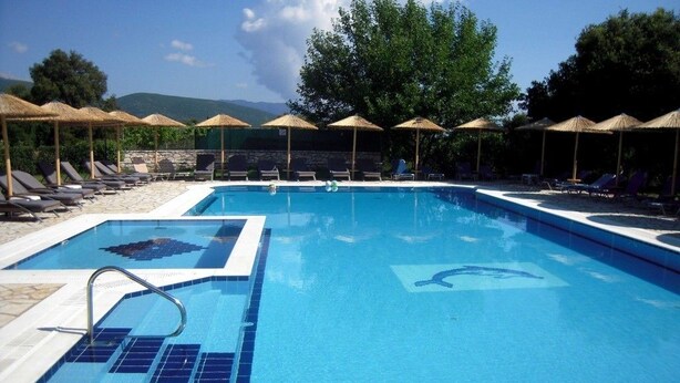 Une piscine entourée d’arbres et d’un mur de pierre, avec des chaises longues et des parasols à proximité.