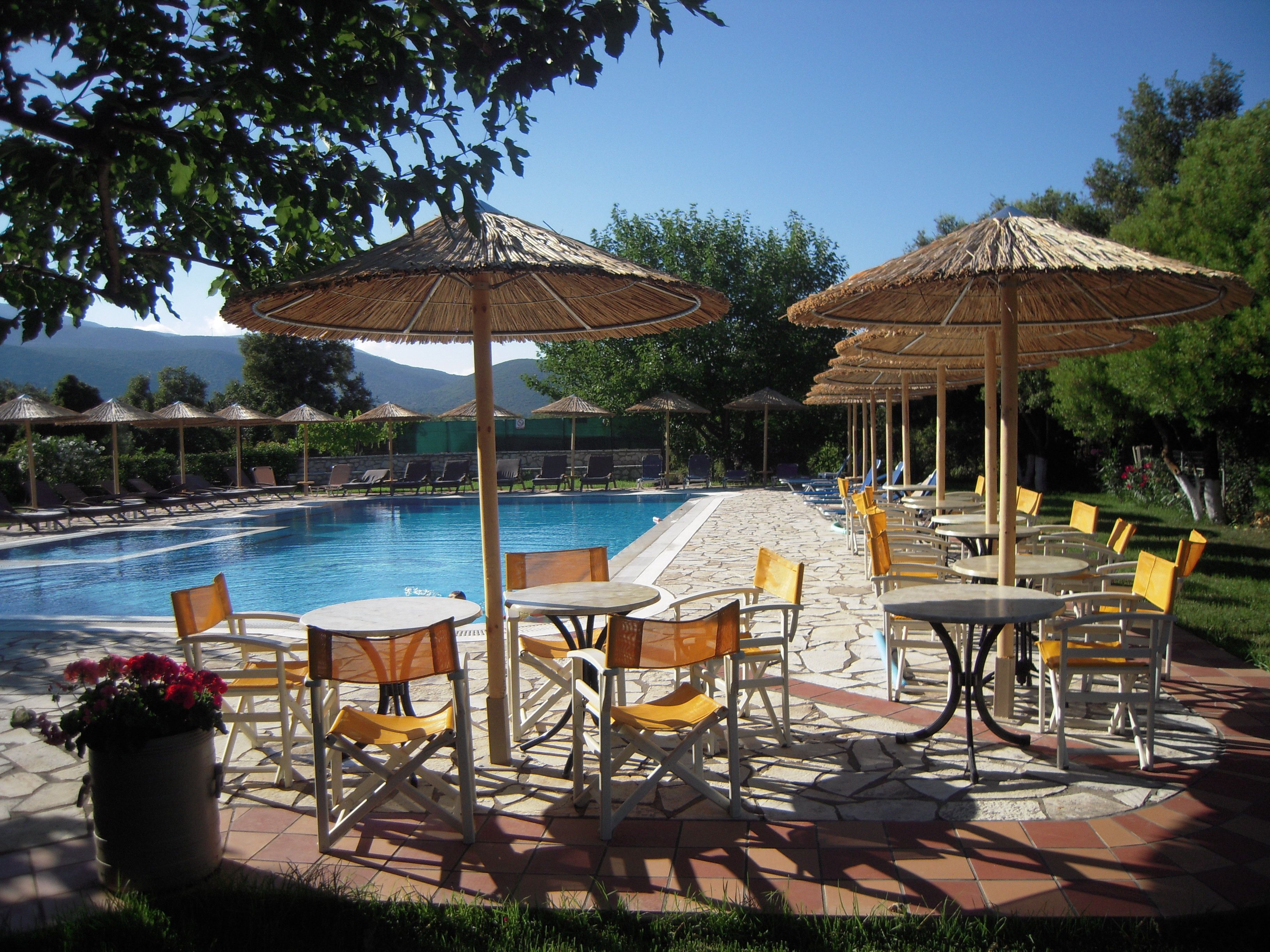 A poolside area with lounge chairs and tables, umbrellas, and a view of mountains in the background.