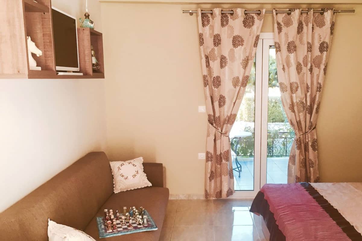 Une chambre à coucher avec un lit, un canapé, une petite table sur laquelle est posé un jeu d’échecs, et une fenêtre avec des rideaux.