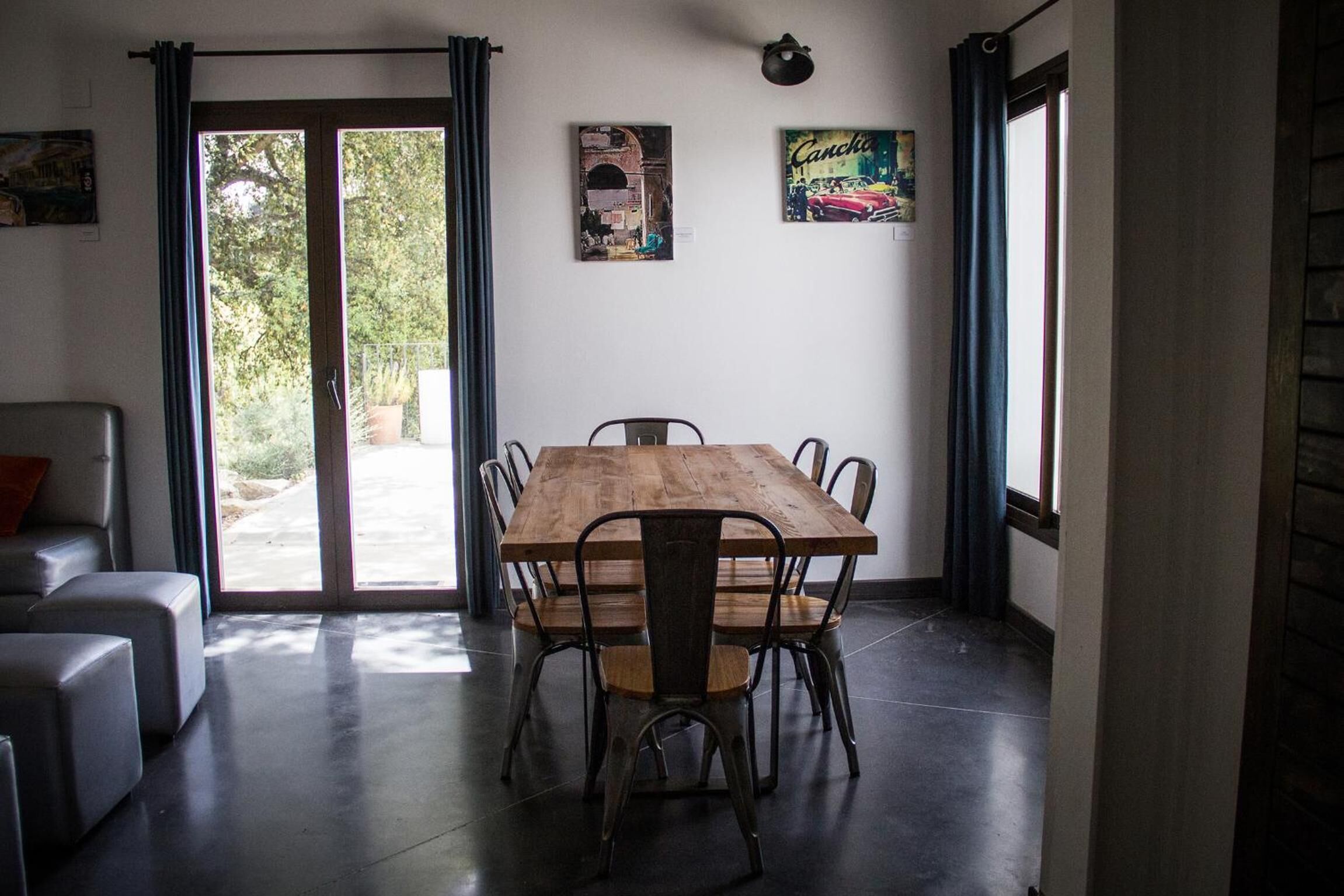 Un coin repas avec une table et des chaises en bois, un canapé et une vue sur l’extérieur, visible à travers une porte vitrée.