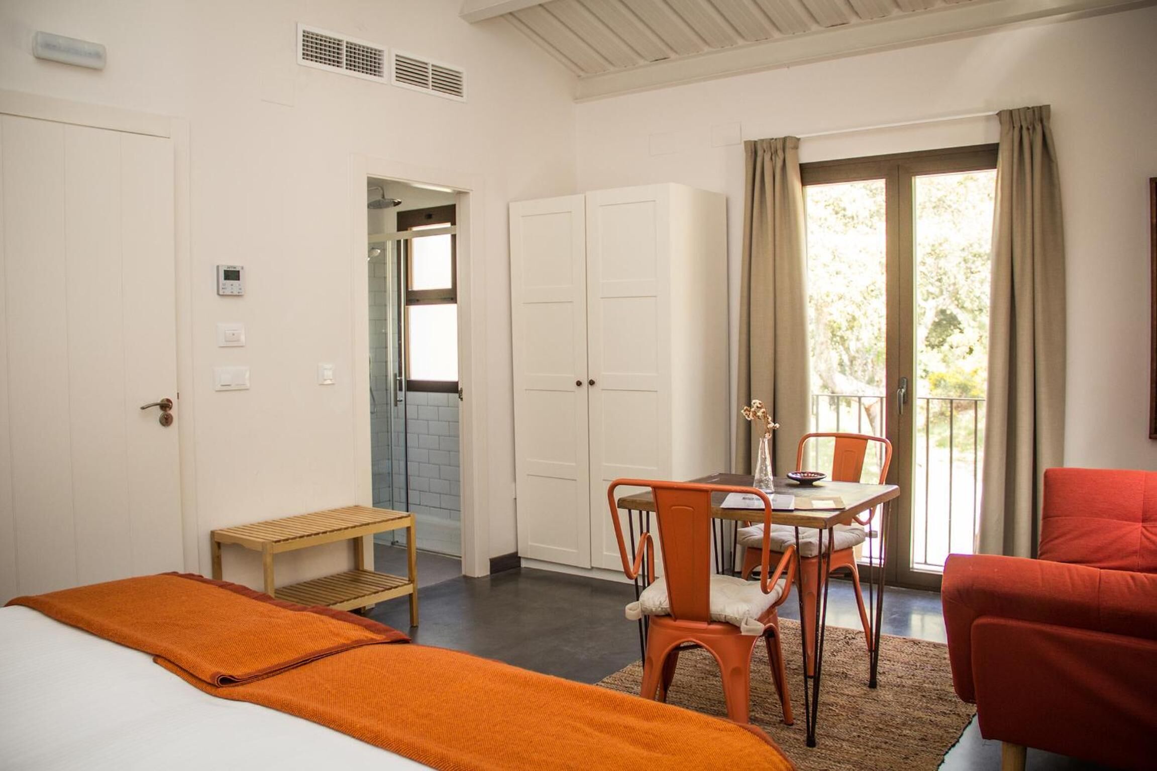Ein Hotelzimmer mit Bett, einem kleinen Tisch mit Stühlen, einem Kleiderschrank und einem Balkon mit Vorhängen.