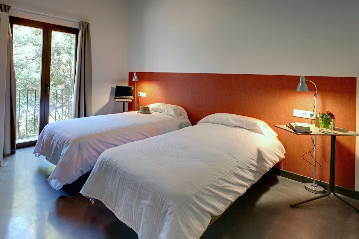 A hotel room with two beds, a TV, a lamp, and a small table with a vase and books.
