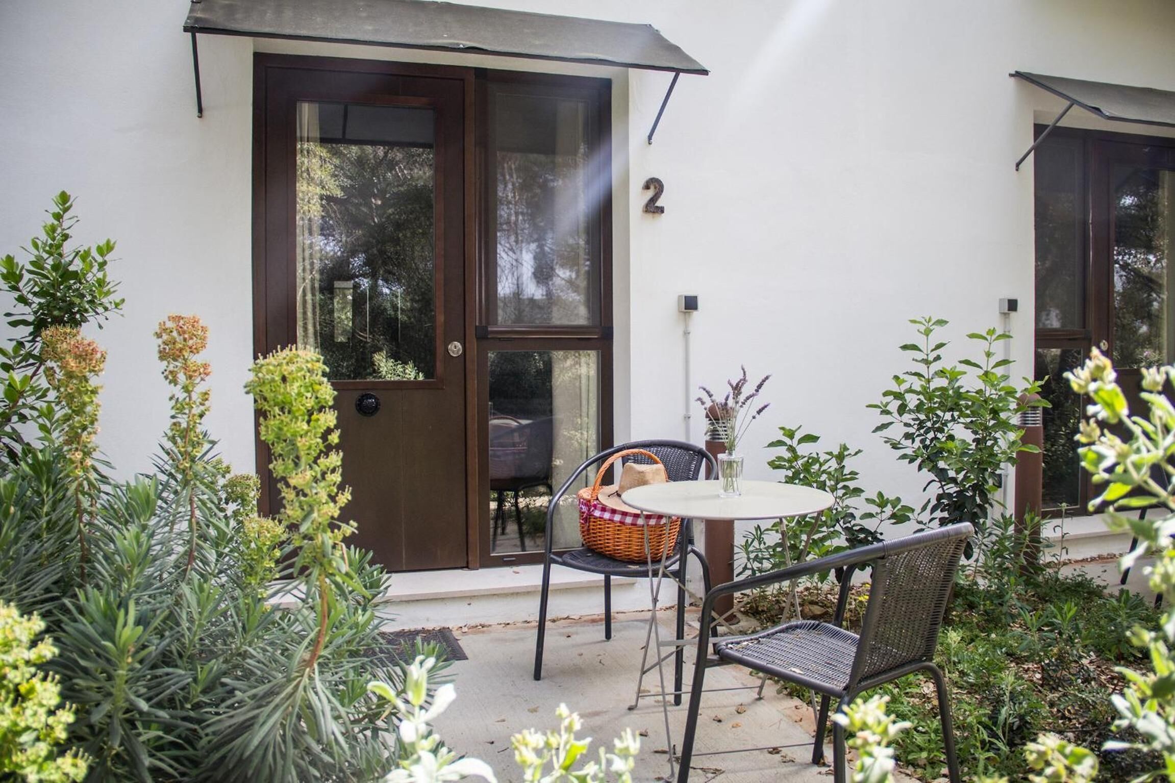 Un patio con mesa y sillas, una puerta con número y diversas plantas.