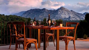A wooden table set with wine glasses and bottles, surrounded by wicker chairs, with a mountainous backdrop. - Tambor del Llano (Grazalema)