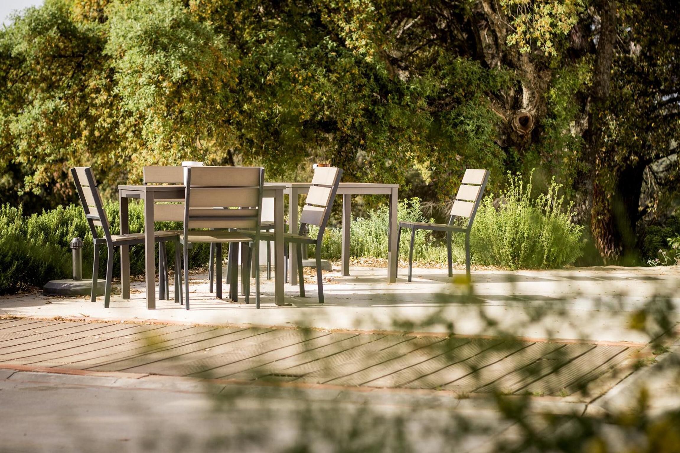 An outdoor seating area with a table and chairs, surrounded by greenery and trees.