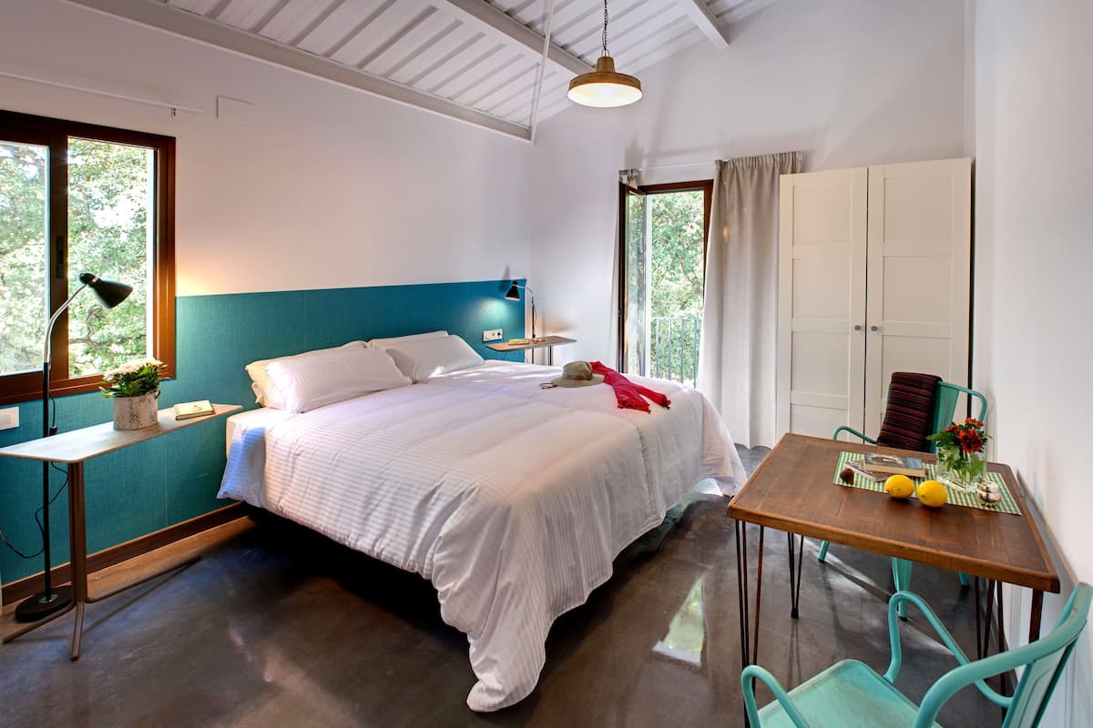 A bedroom with a bed, bedside table, lamp, window, and a small table with a vase and lemons.