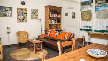A cozy living room with a brown sofa, a wooden bookshelf, and a dining table with a bowl and a glass.