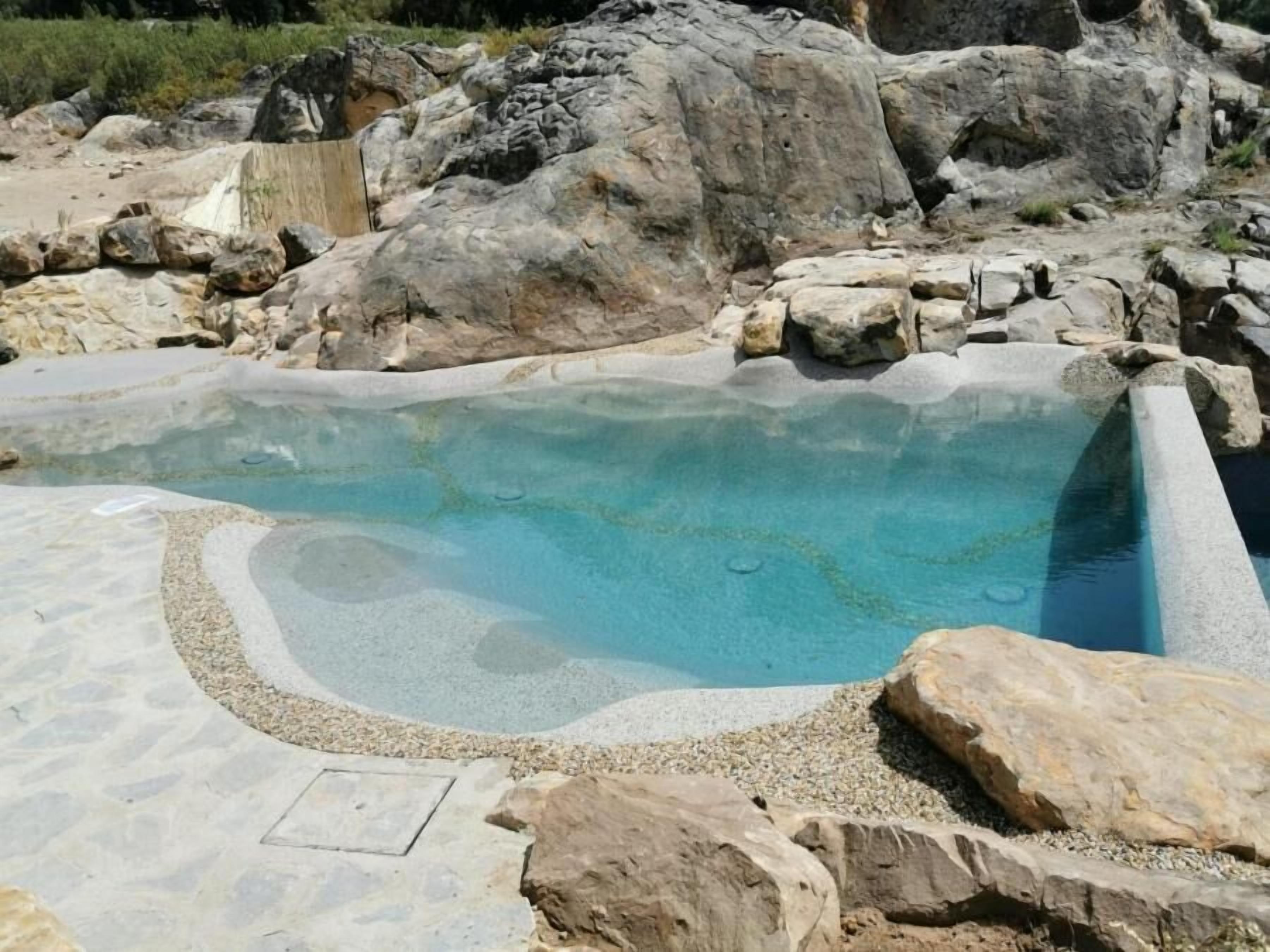 Ein Thermalbecken mit klarem Wasser, umgeben von großen Steinen und Kieselsteinen.