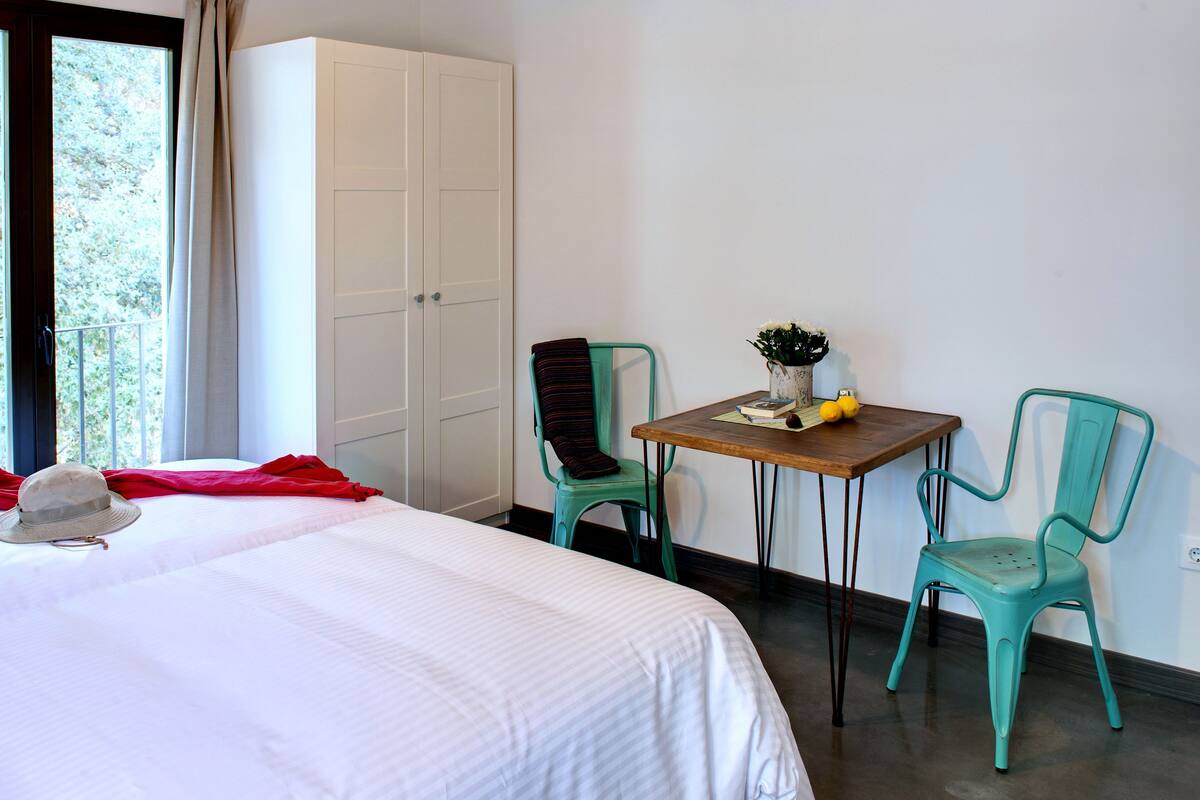 A hotel room with a bed, a table with chairs, a wardrobe, and a window with curtains.