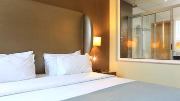 Une chambre d’hôtel avec un grand lit, une table de chevet avec une lampe et une vue sur l’espace douche.