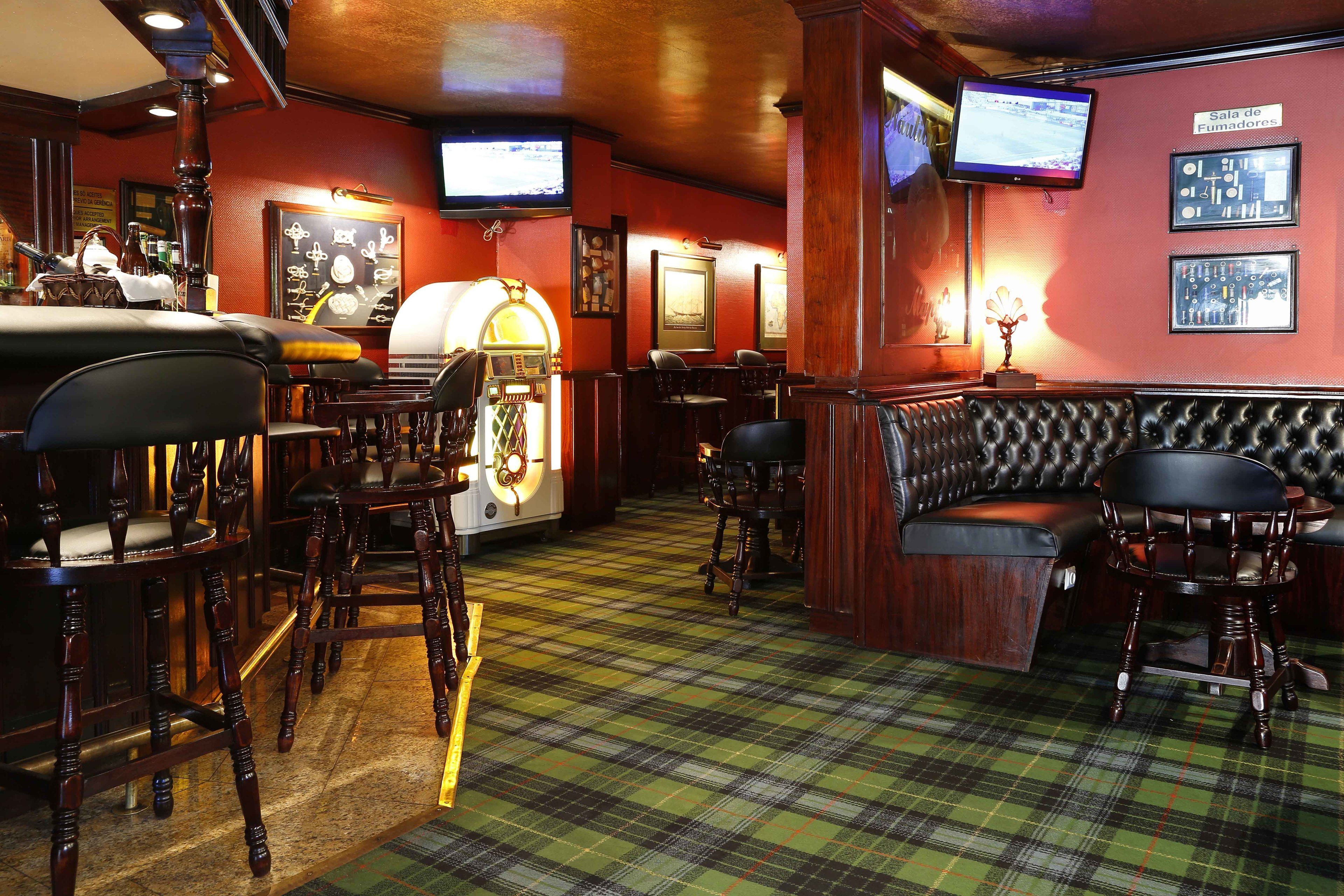 A bar area with wooden chairs, a bar counter, a jukebox, and a television screen.
