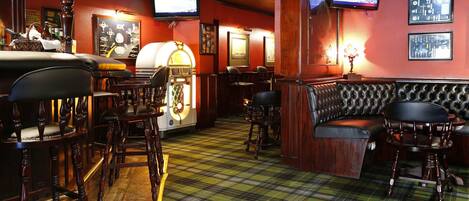 A bar area with wooden chairs, a bar counter, a jukebox, and a television screen.