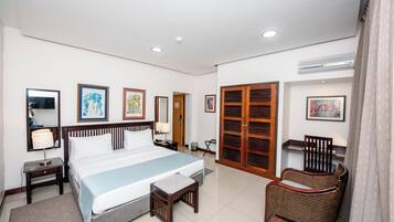 Una habitación de hotel con una cama grande, mesitas de noche, una silla, un armario y cuadros en las paredes.