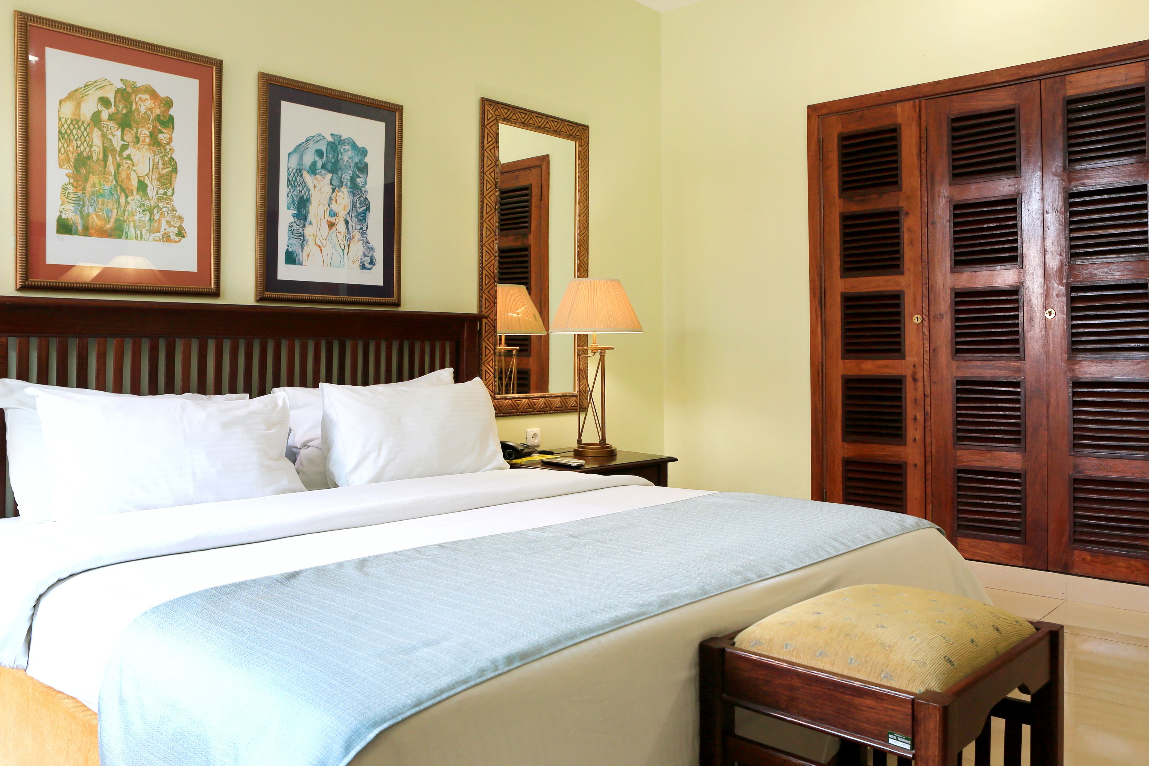 A hotel room with a large bed, a bedside table with a lamp, and a wooden wardrobe.