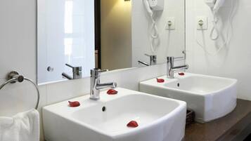Une salle de bain avec deux lavabos, un grand miroir et des sèche-cheveux fixés au mur.