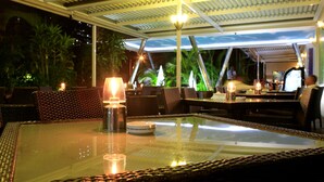 An outdoor dining area with wicker furniture, glass tables, and ambient lighting. - Hotel Terminus (Maputo)