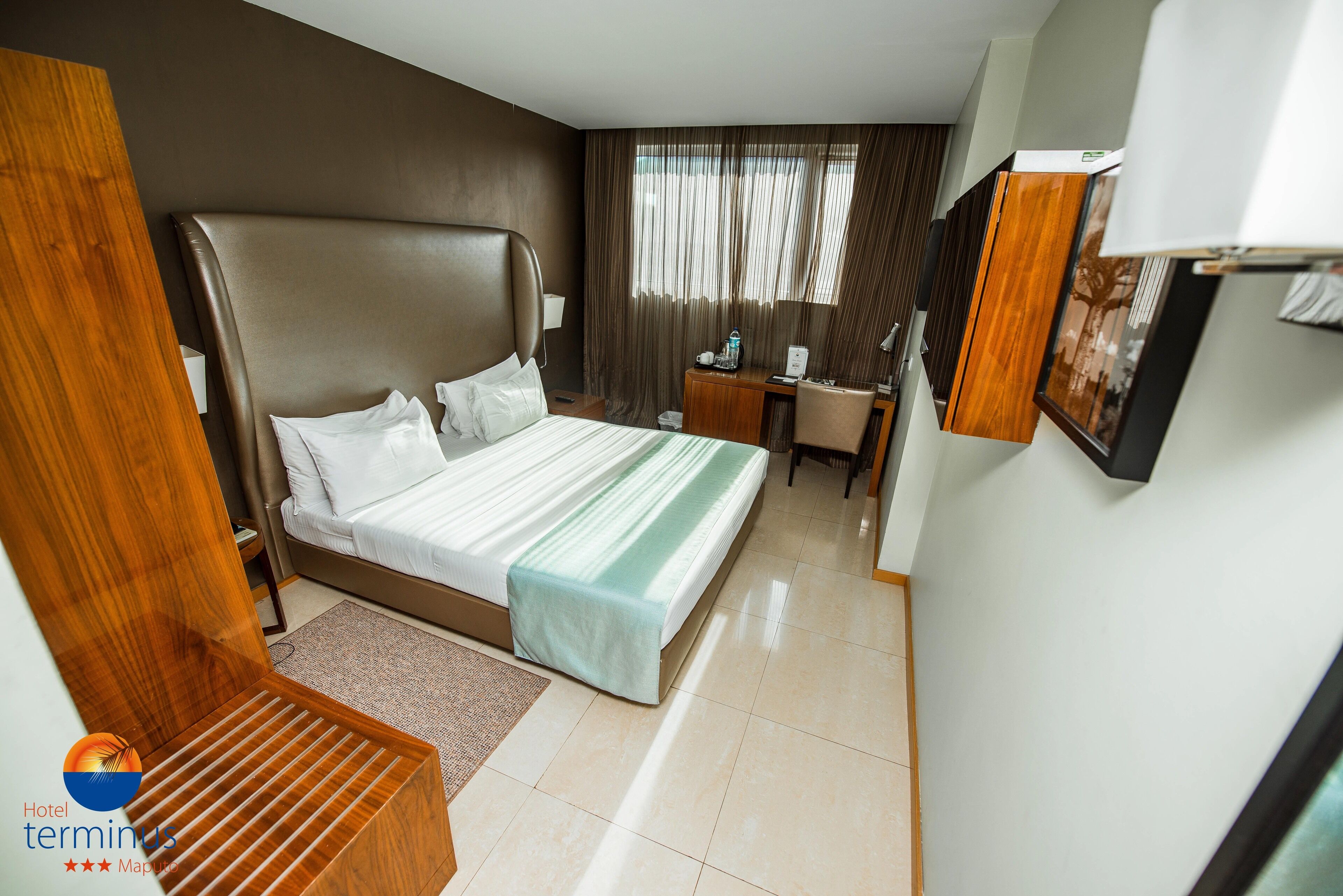 A hotel room with a large bed, a desk, a chair, and a small table.