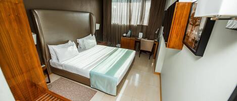 A hotel room with a large bed, a desk, a chair, and a small table.