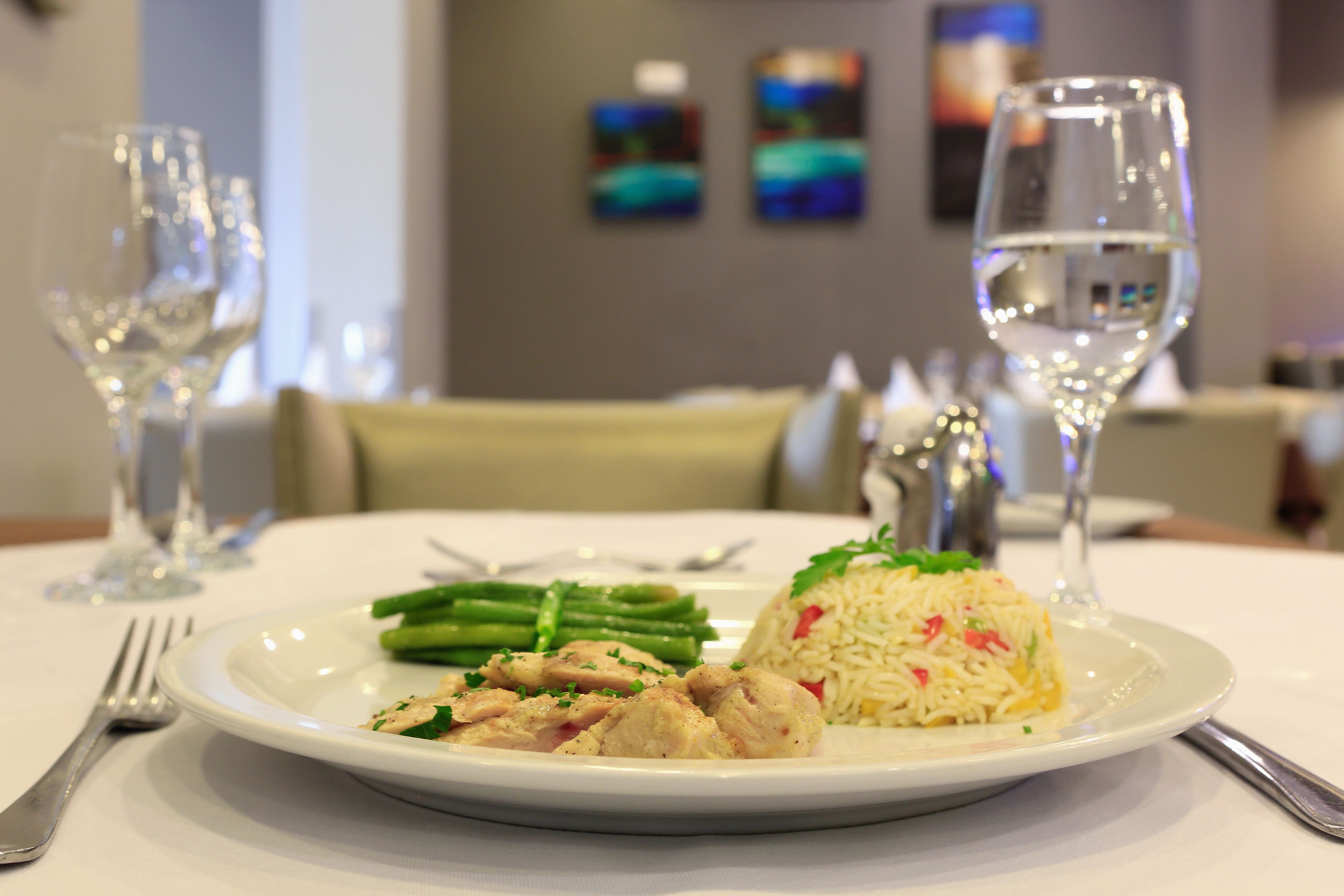 A plate of food with rice, chicken, and asparagus on a table with a wine glass and cutlery.