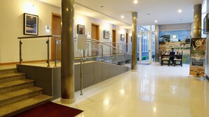 A hotel lobby with a staircase, a reception desk, and a large poster advertising safaris and beaches. - Hotel Terminus (Maputo)