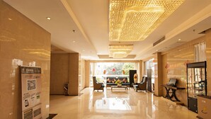 A spacious lobby with a polished floor, a seating area with sofas, a coffee machine, and a decorative ceiling light fixture.