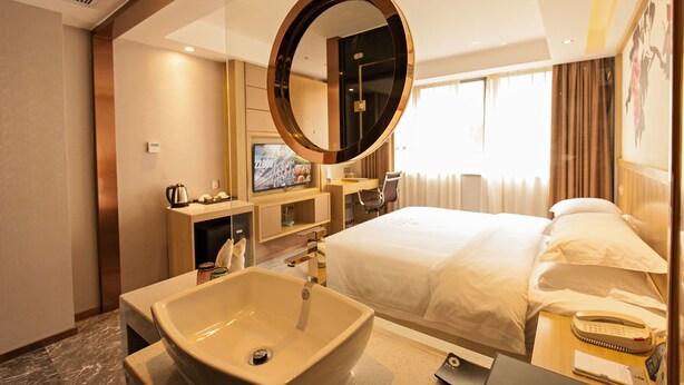 A hotel room with a large bed, a round mirror, a sink, a television, and a desk with a chair.