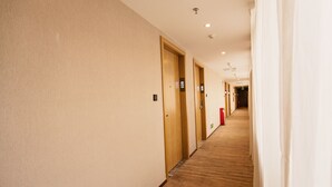 A hotel hallway with carpeted floors, wooden doors, and a red fire extinguisher.
