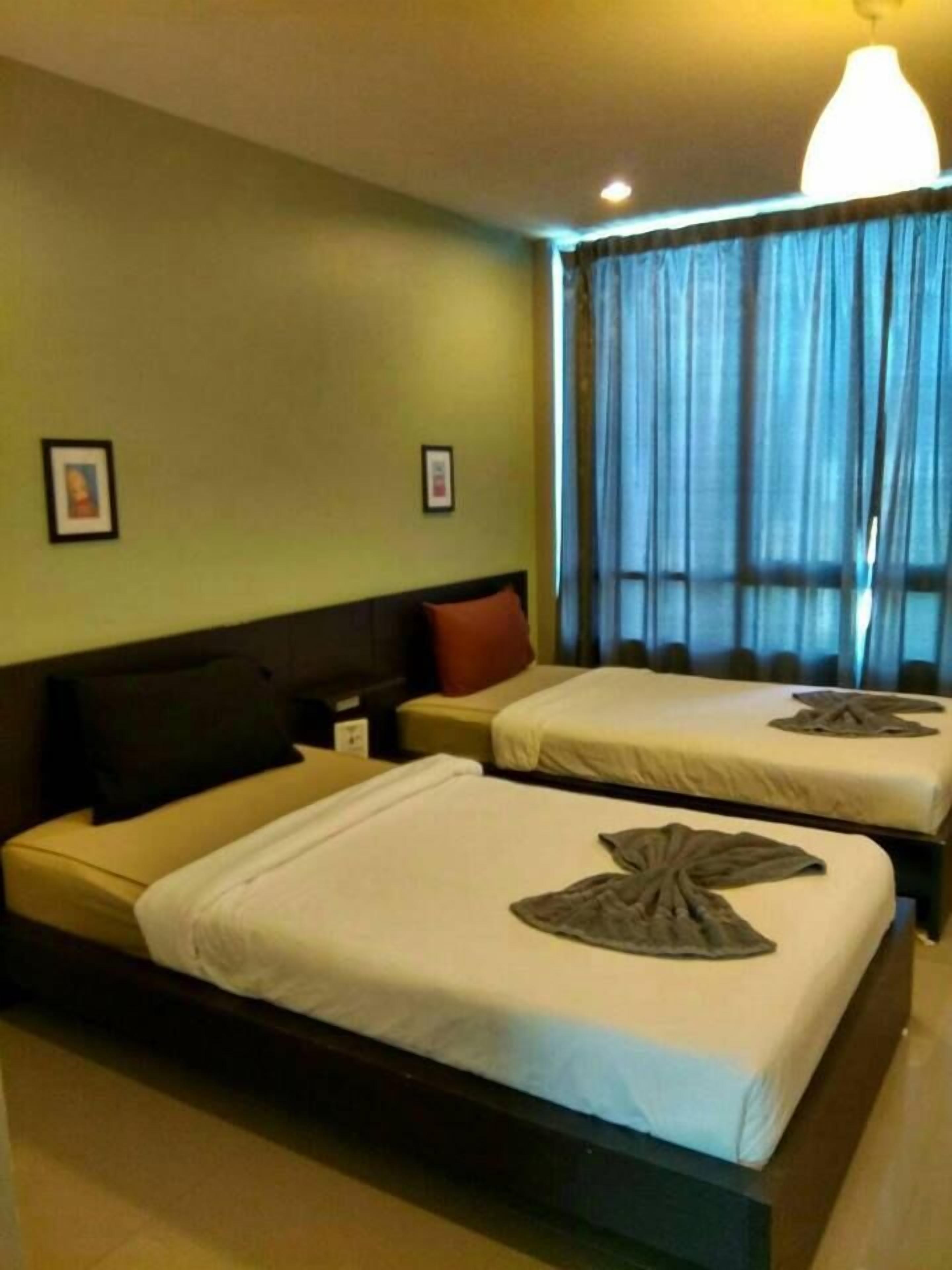 Een hotelkamer met twee bedden, een nachtkastje, een lamp en een raam met gordijnen.