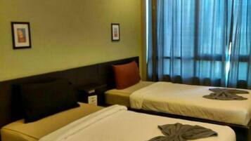 Een hotelkamer met twee bedden, een nachtkastje, een lamp en een raam met gordijnen.