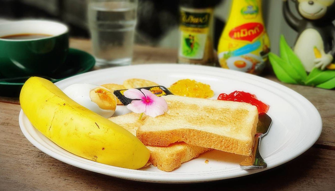 Une assiette contenant une banane, des toasts et un petit dessert, posée sur une table en bois.