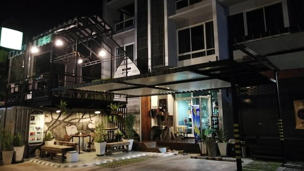 A modern building with a covered outdoor seating area, potted plants, and a staircase leading to an upper level. - White Monkey Guesthouse (Phetchaburi)