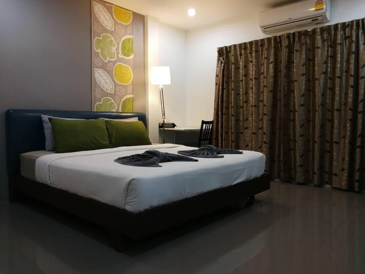 Habitación de hotel con cama, escritorio, silla, aire acondicionado y una pared con diseño de hojas.