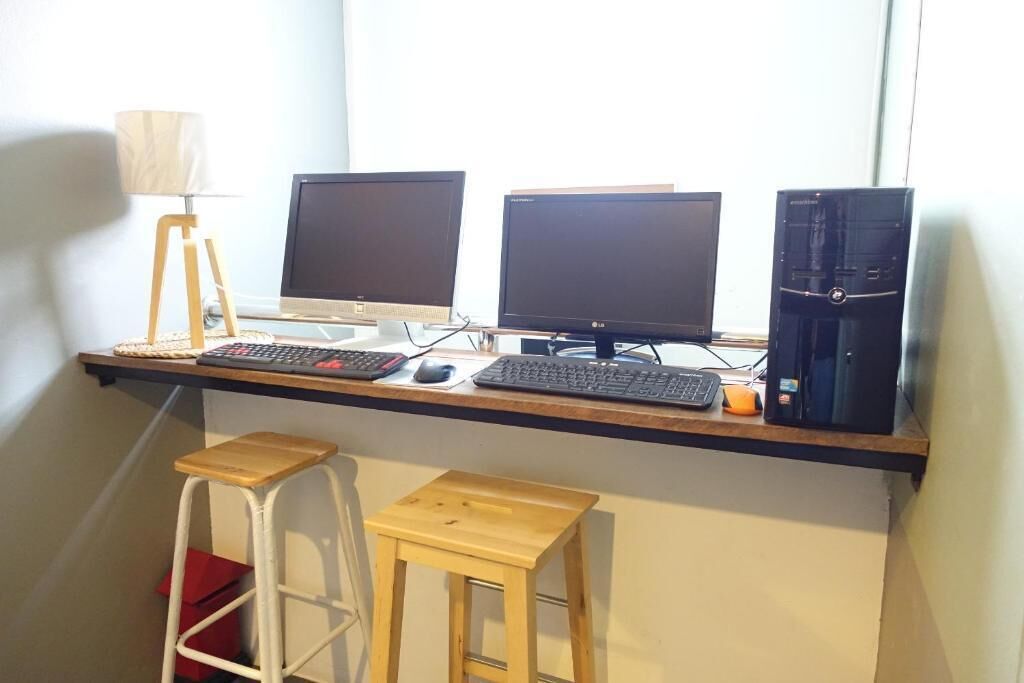Un espacio de trabajo con tres monitores, una computadora de escritorio y dos taburetes de madera.