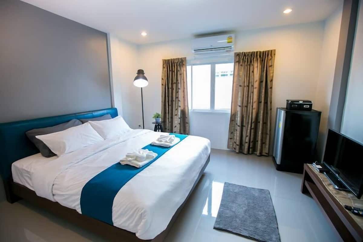 A hotel room with a bed, a flat-screen TV, a desk with a computer, and a window with curtains.