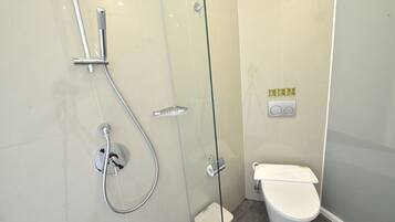 A modern bathroom with a glass-enclosed shower, a toilet, and a small trash bin.
