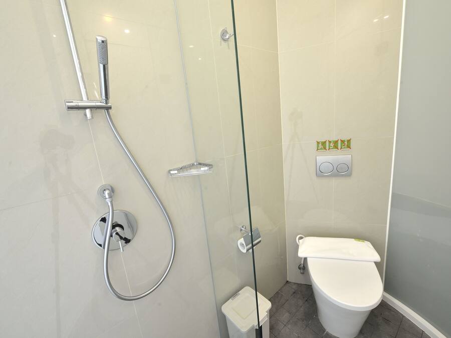 A modern bathroom with a glass-enclosed shower, a toilet, and a small trash bin.