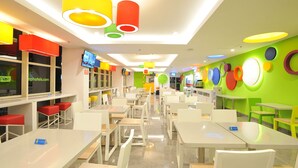 A brightly lit indoor space with white tables and chairs, colorful hanging lamps, and a green wall with circular decorations. - POP! Hotel Diponegoro Surabaya (Surabaya)