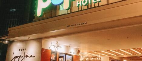 Entrada de un hotel con un letrero de neón que dice "POP HOTEL" y un mostrador de recepción a la vista.