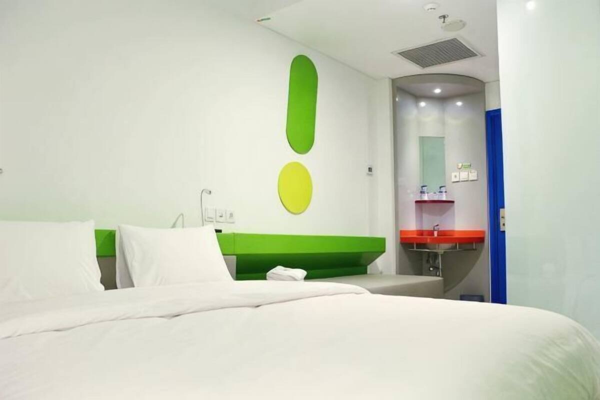 Hotellihuone, jossa on sänky, vihreä tehosteseinä, valkoinen pesuallas ja peili.