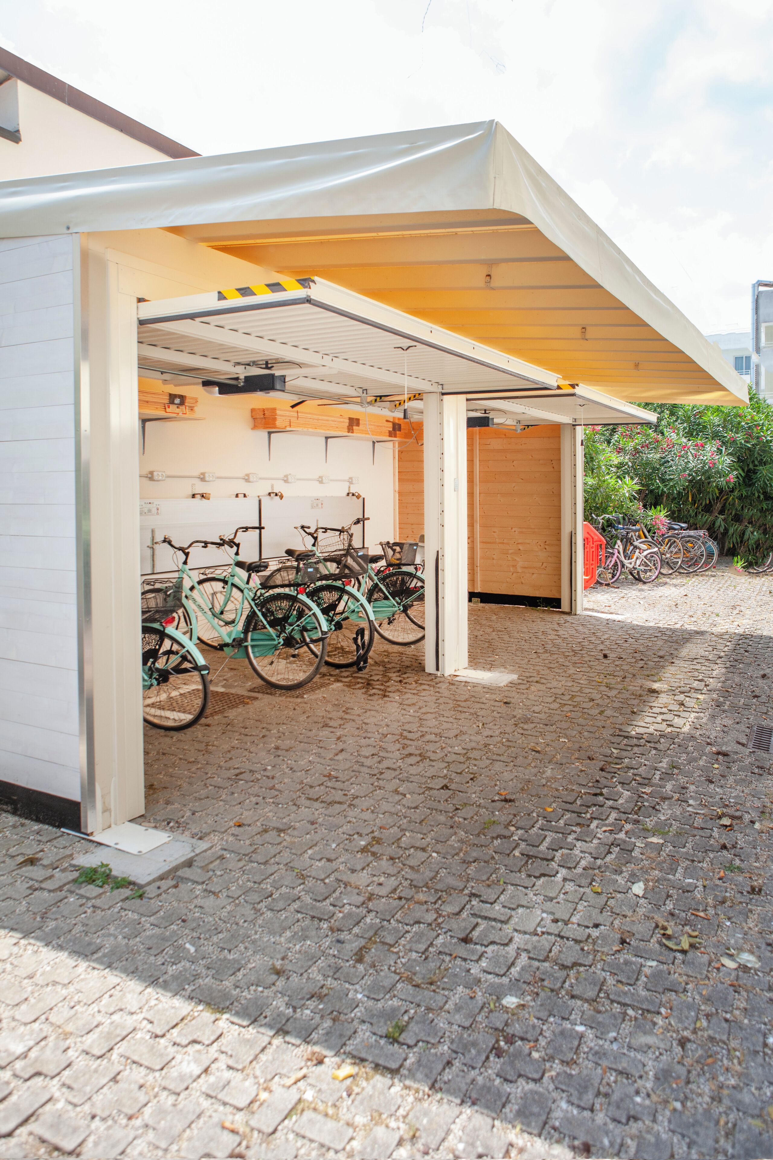 Een overdekte fietsenstallingsruimte met meerdere fietsen, een grond van bakstenen en een gebouw-ingang.