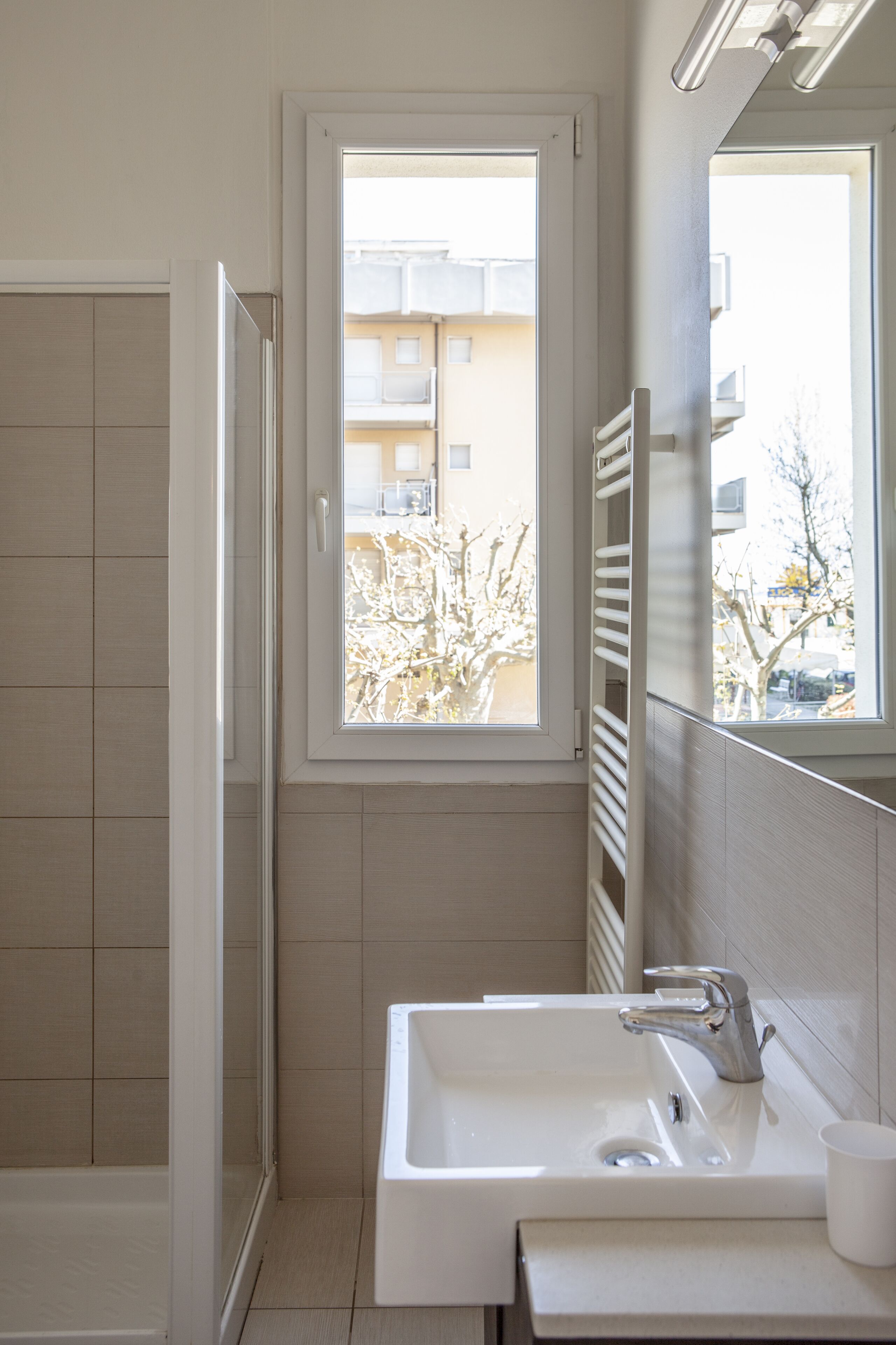 A bathroom with a white sink, a mirror, and a window.