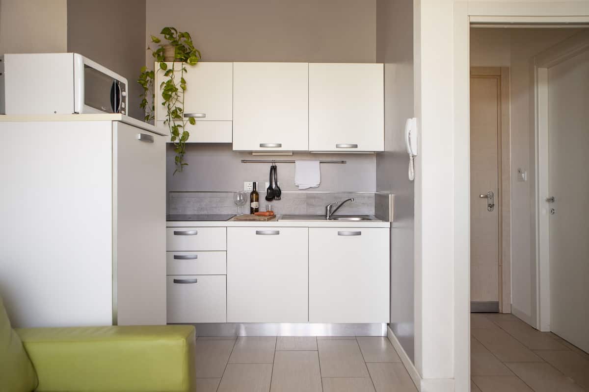 Une cuisine moderne avec des meubles blancs, un four à micro-ondes, un évier et une chaise verte.