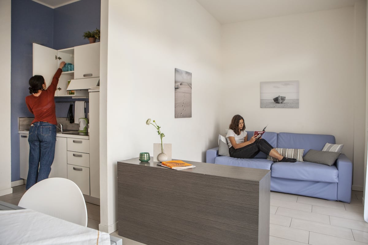 Un salon moderne comprenant un canapé, un coin repas avec une table et un espace cuisine avec des placards.