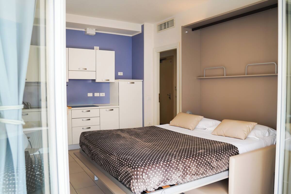 Une chambre avec un lit, un bureau et une kitchenette.