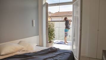 Una camera da letto con un letto, cuscini, una pianta in vaso e un balcone con una persona.