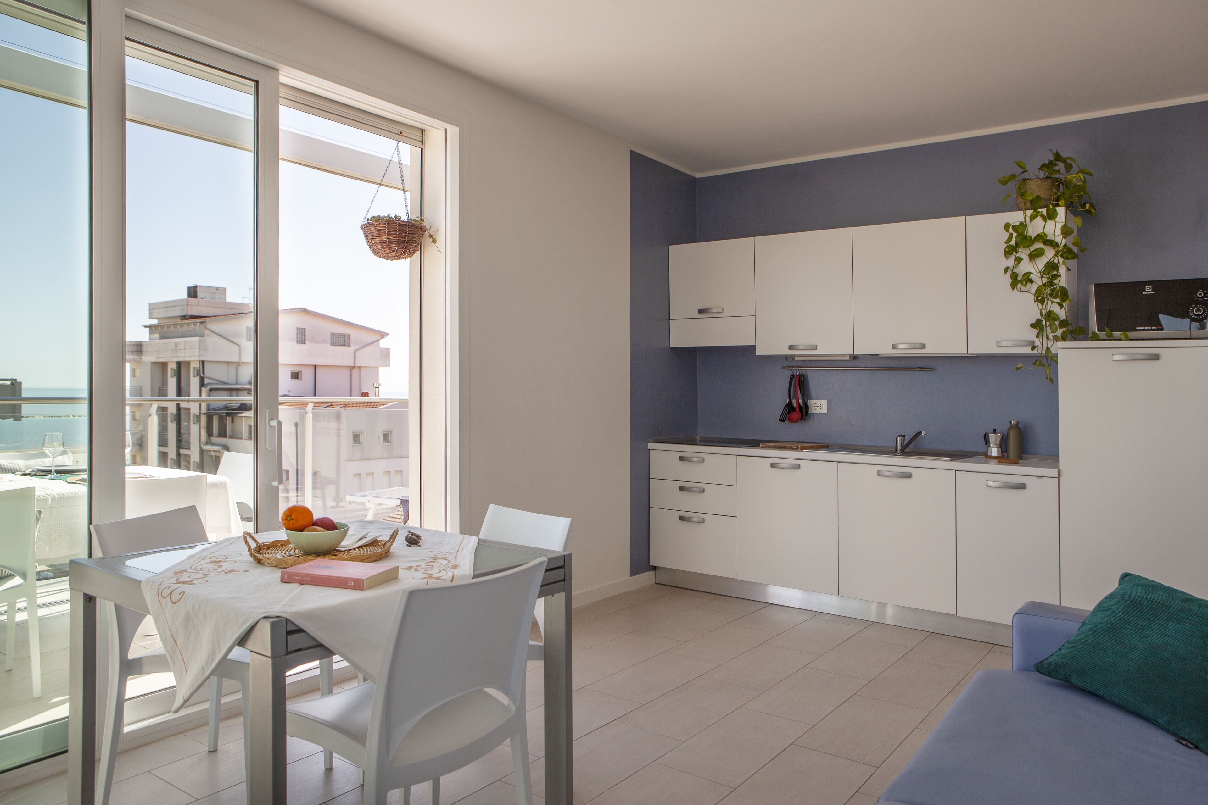 A modern kitchen with white cabinets, a dining area with a table and chairs, and a view of the sea through large windows.