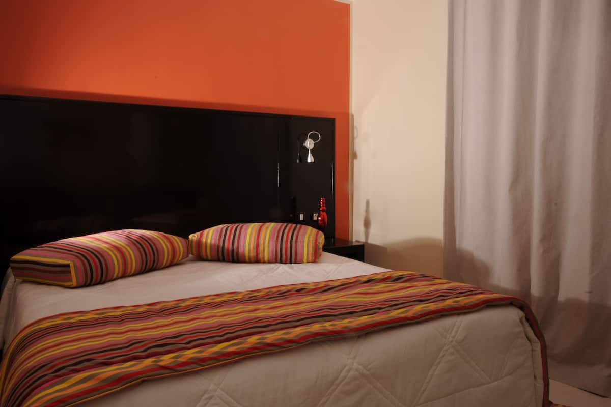 A bed with striped bedding, a black headboard, and a red accent wall.