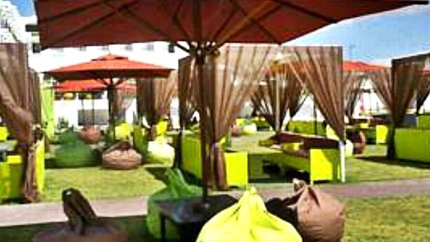 An outdoor seating area with multiple red umbrellas, green chairs, and bean bags. - Freedom Hôtel Club (Hammamet)