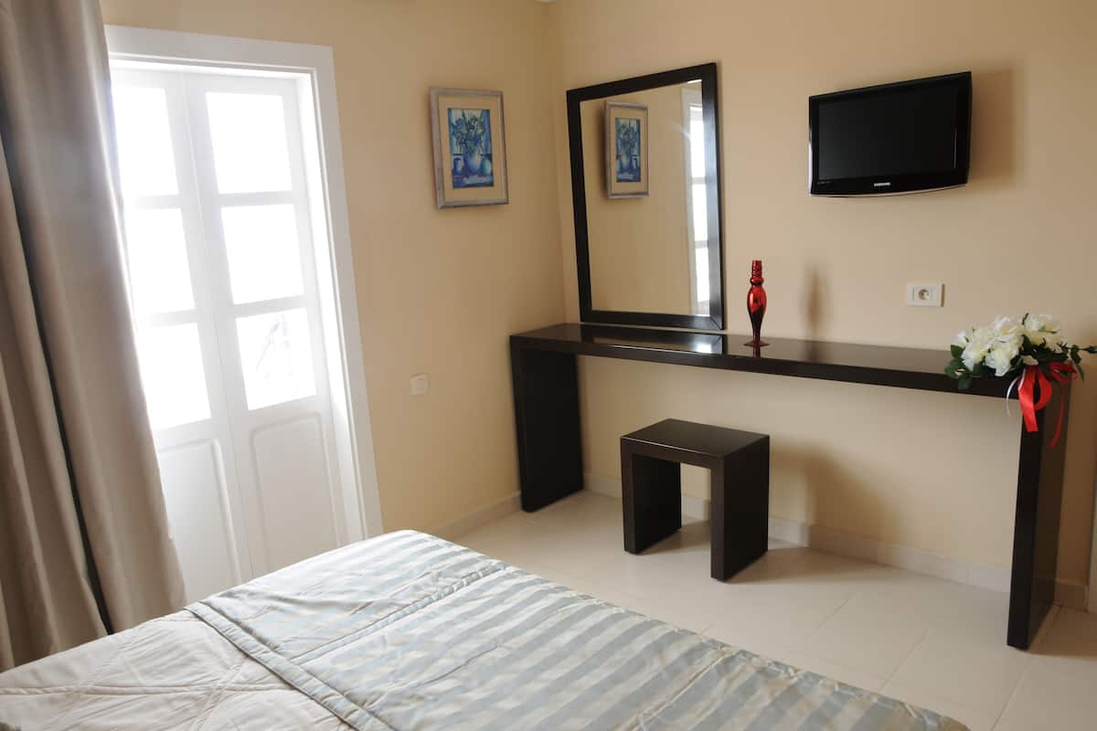 A bedroom with a bed, a desk, a chair, a TV, and a door.