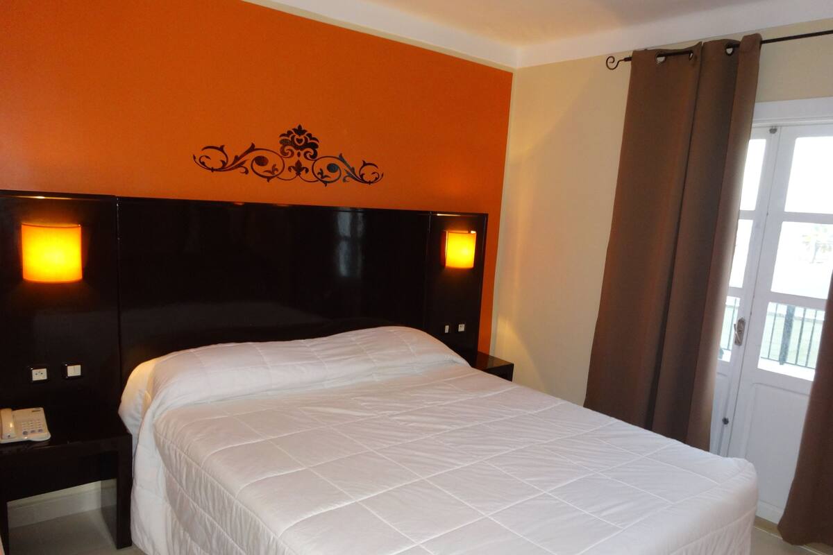 A hotel room with a large bed, two bedside tables, and a headboard with wall-mounted lights.